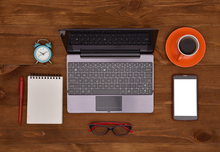 Laptop cellphone glasses note pad and cup of coffee on wooden table Stock Photo