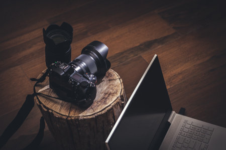 Camera with lens on tree trunk and laptop in dark and rustic environment Stock Photo