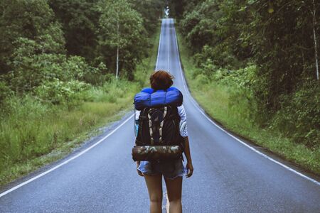 Freedom traveler woman standing with raised arms and enjoying a beautiful nature on a country road woman with backpack travel in the countryside on a mountain