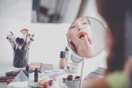 Young beautiful woman making make up near mirror sitting at the desk