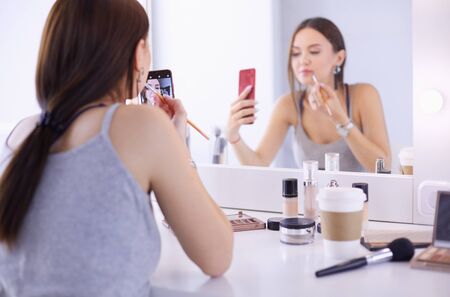 Beauty blogger filming makeup tutorial with smartphone in front of mirror