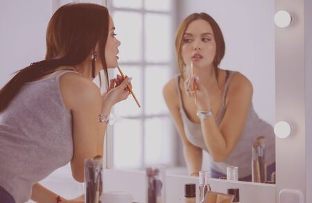 Young woman applying lipstick in front of a mirror