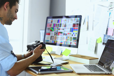 Portrait of young designer sitting at graphic studio in front of laptop and computer while working online