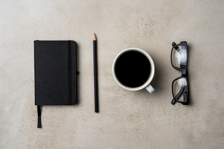 Office desktop with coffee cup pencil notebook and glasses