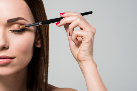 Young beautiful woman applying eyeshadows isolated on grey