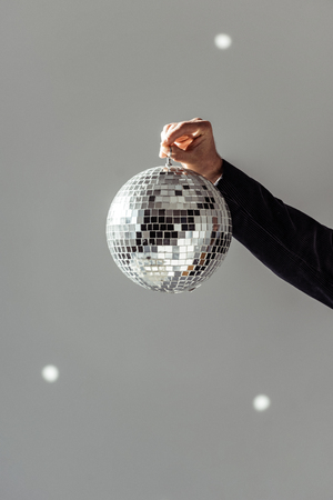 Cropped view of man holding disco ball on grey background