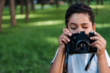 African american boy holding digital camera while talking photo in park