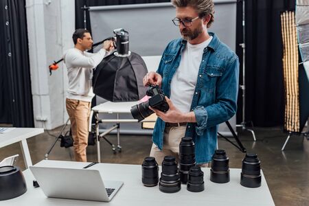 Bearded photographer holding digital camera near laptop on table