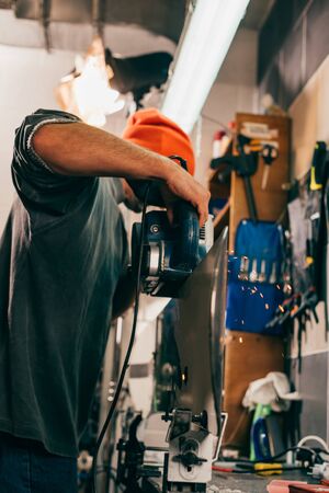 Worker repairing snowboard with belt sander in repair shop