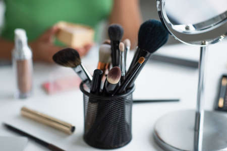 Cropped view of cosmetic brushes near mirror and blurred african american woman