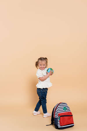 niño feliz con síndrome de down sosteniendo un globo pequeño cerca de la mochila en beige