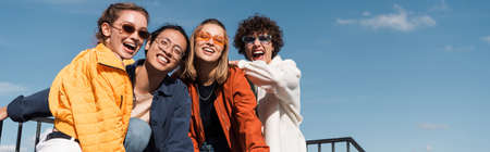 Alegres amigos multiculturales con elegantes gafas de sol mirando la cámara al aire libre, pancarta Foto de archivo