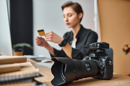 Focus on camera on table next to young blurred female photographer paying online with credit card Stock Photo