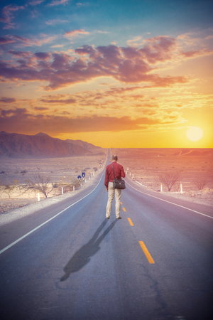 A man walks on the highway at sunset in the desert