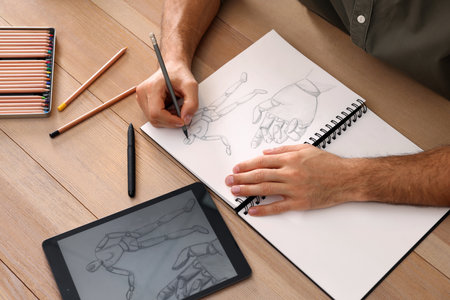 Man drawing in sketchbook with pencil at wooden table closeup Stock Photo