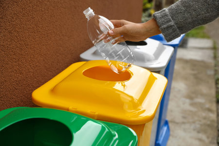 Mujer arrojando una botella de plástico a un contenedor de reciclaje al aire libre primer plano