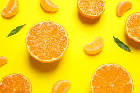 Flat lay composition with halves of fresh ripe tangerines and leaves on yellow background citrus fruits