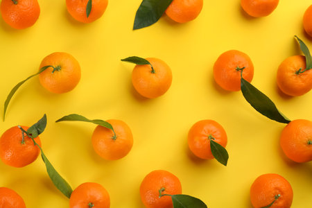 Fresh tangerines with green leaves on yellow background flat lay