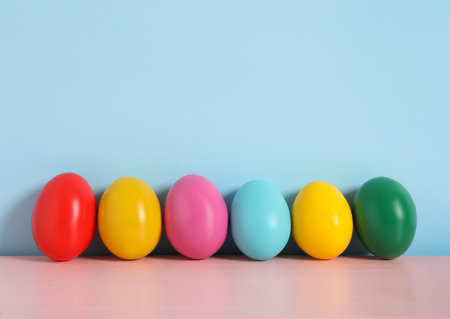 Easter eggs on pink wooden table against light blue background space for text