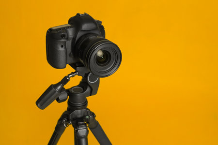 Modern tripod with professional camera on yellow background space for text Stock Photo