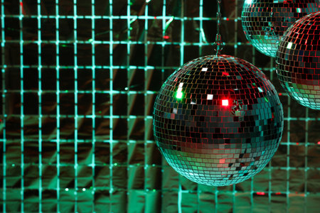 Shiny disco balls against foil party curtain under color lights space for text