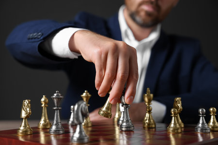 Man with game pieces playing chess at checkerboard against dark background closeup