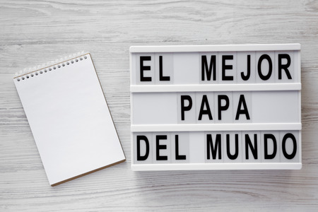 Palabras de 'El Mejor Papa Del Mundo' en tablero moderno, Bloc de notas en blanco sobre fondo blanco de madera, vista superior. Arriba, desde arriba, plano. Concepto del día del padre. Foto de archivo