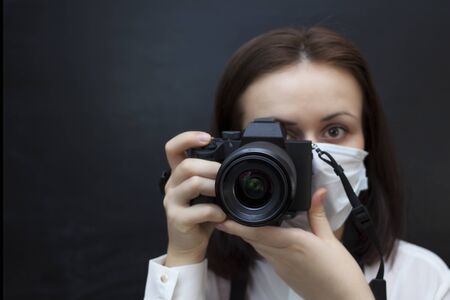 Girl photographer in a medical protective mask chalk board background in the background the concept of working from home during the quarantine