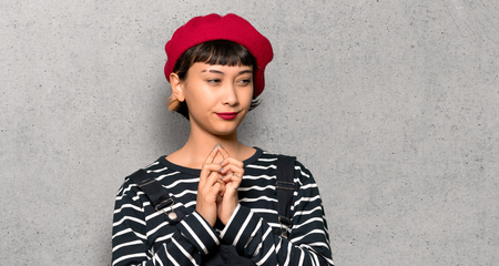 Young woman with beret scheming something over textured wall