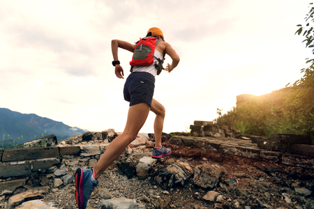 Young woman trail runner running at great wall on the top of mountain Stock Photo