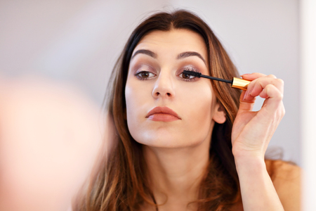 Attractive young woman doing make up while looking at the mirror in bathroom