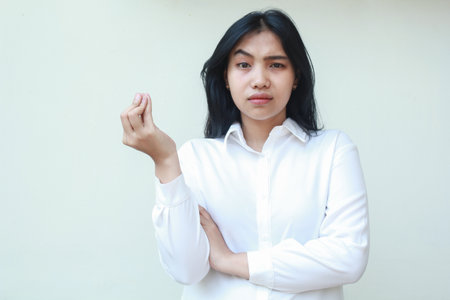 Portrait of confused asian young business woman manager looking at camera wondering with raising arm and curled up fingers wearing white formal shirt standing questioning disbelief gesture Фото со стока