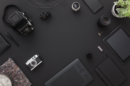 Work space on black table of a creative designer or photographer with laptop tablet cameras other objects of inspiration and copy space stylish home studio concept of technology trends