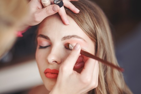 Professional beautician artist applying makeup on young model