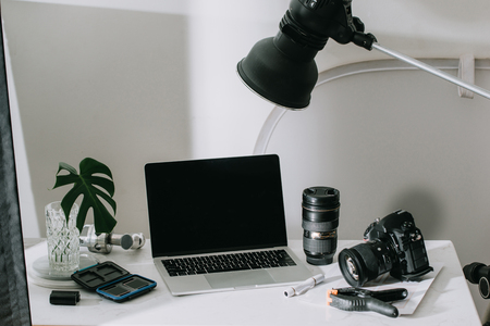 Still life working from home desk with professional photographic equipment camera lens computer monitor electronics indoors