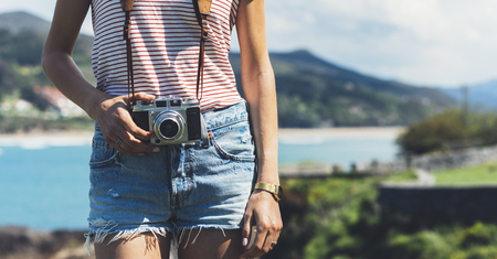 Tourist traveler photographer making pictures sea scape on vintage photo camera on background ocean hipster girl enjoying peak mountain and nature holiday mock up ocean waves view blurred backdrop Stock Photo