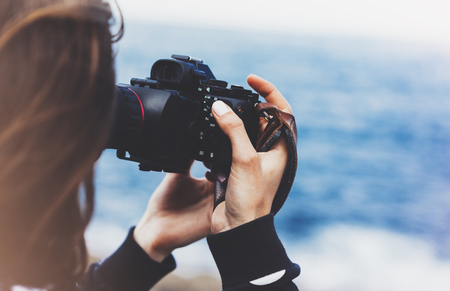 Tourist traveler photographer girl taking pictures of seascape on modern photo camera on background blue ocean view mockup sun flare hipster female hands shoots video nature holiday concept