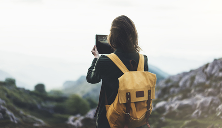 Hipster girl with backpack enjoying sunset on peak mountain tourist traveler taking pictures landscape on mobile phone Stock Photo