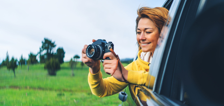 Smile tourist girl in an open window of a auto car taking photography click on retro vintage photo camera photographer looking on camera technology blogger using hobby content concept enjoy trip Stock Photo