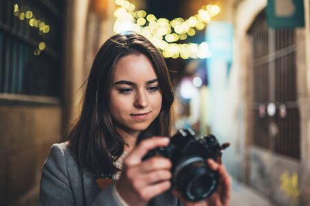 Photographer girl with retro camera take photo on background bokeh light in night city tourist travels in barcelona photo hobby outdoor portrait of young smile woman with video technology