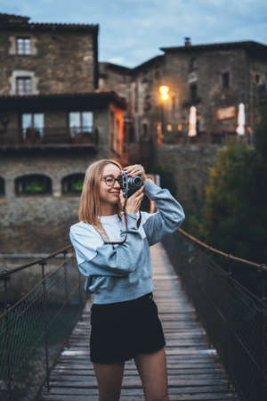 blond toeristisch meisje staat op hangbrug wandelen oude historische stad en maakt foto's met retro camera, schattige jonge hipster genieten van een weekend vakantie in de zomer maakt gebruik van fotocamera om foto's van haar reis te maken