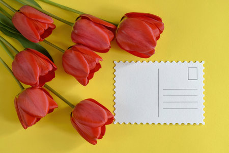 Bouquet of fresh red tulips and greeting card on yellow background top view mock up close up copy space selective focus