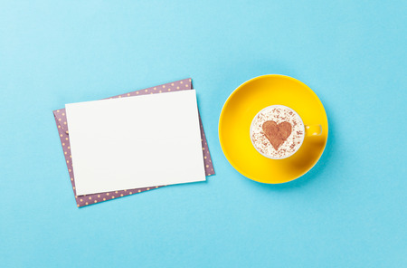 Taza de cappuccino con forma de corazón y el sobre en el fondo azul.