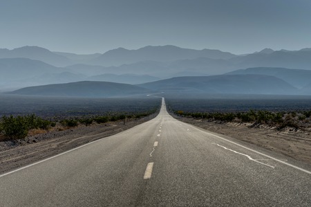 Empty street towards blue mountains and sky in death valley national park