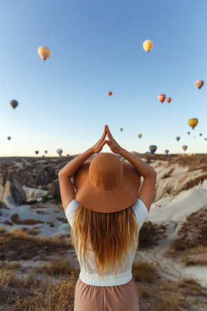 Young attractive girl stands on the mountain with flying air balloons on the background cappadocia