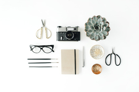 Feminini desk workspace with succulent retro camera scissors diary glasses and golden clips on white background flat lay top view