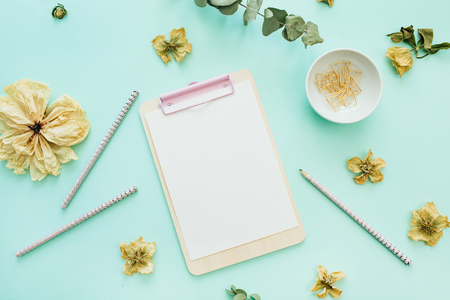 Flat lay home office desk workspace with clipboard flowers and branches on blue background top view minimal mock up Stock Photo