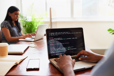 Over the shoulder shot of young male developer typing code on laptop in office