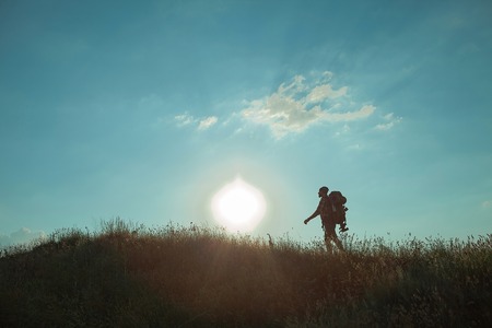 Young caucasian tourist with backpack walking on a green meadow at sunset