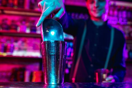 Close up of professional barman finishes preparation of alcoholic cocktail in multicolored neon light gives it to client entertainment drinks service concept modern bar trendy neoned colors